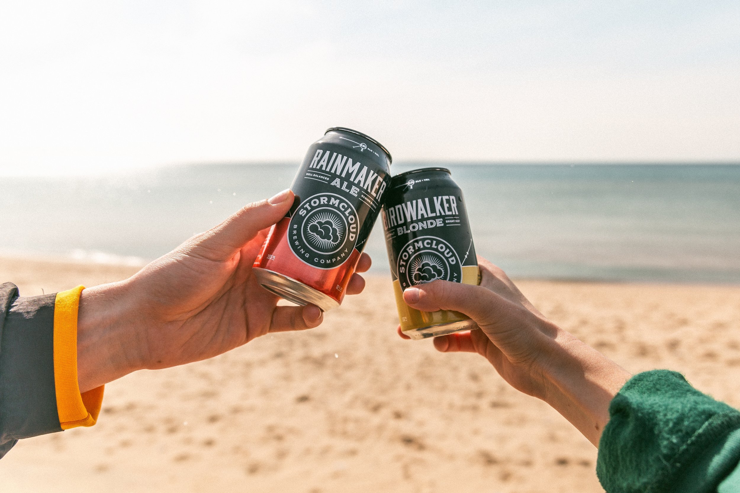 two hands toasting with cans on the beach